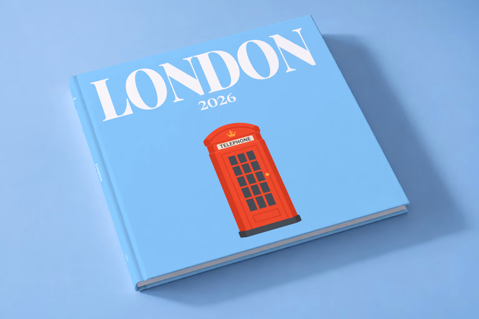 London square hardcover photo book with the illustrated cover of a red London telephone box on sky blue, lying on a pale blue studio backdrop