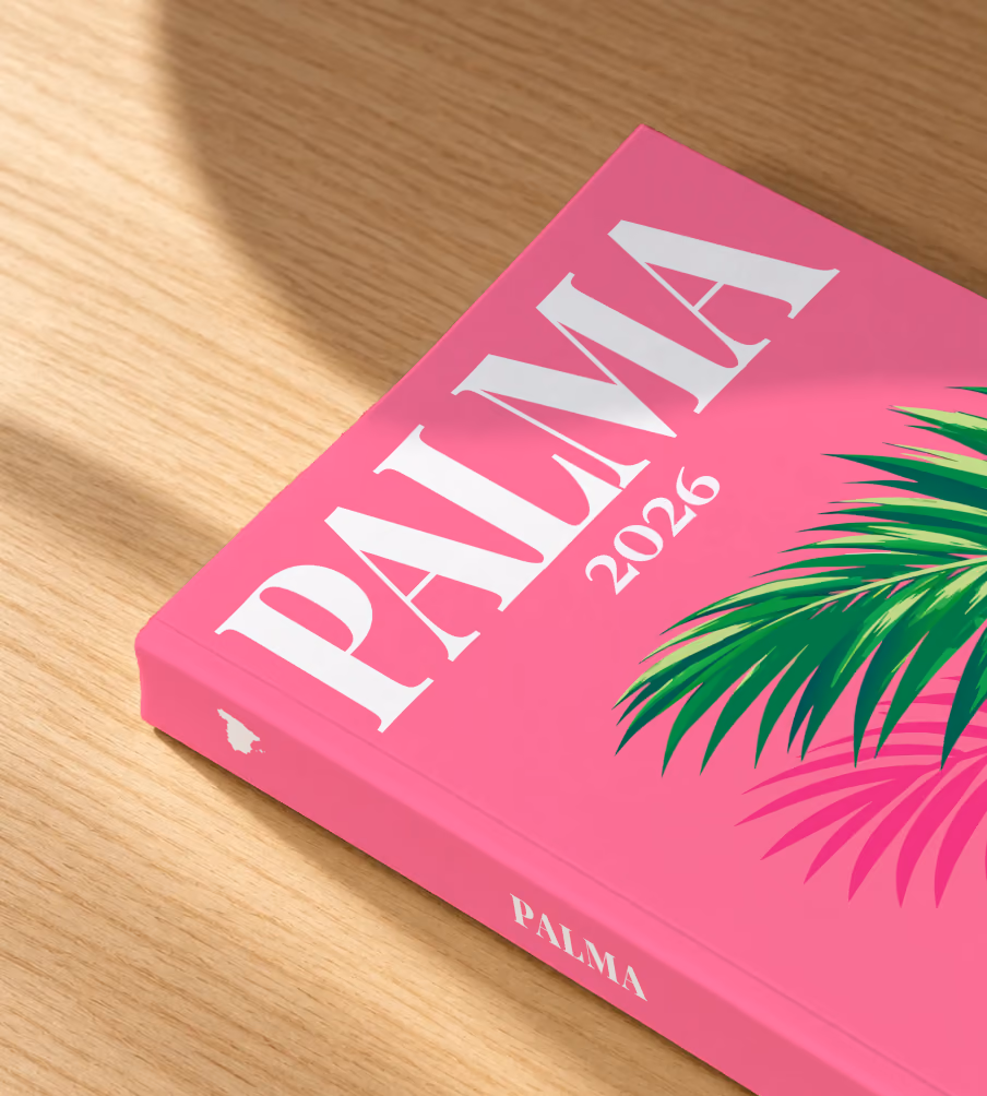 Mallorca softcover photo book with the Palma illustrated cover of a palm frond on hot pink, lying on an oak desk in dappled afternoon sunlight
