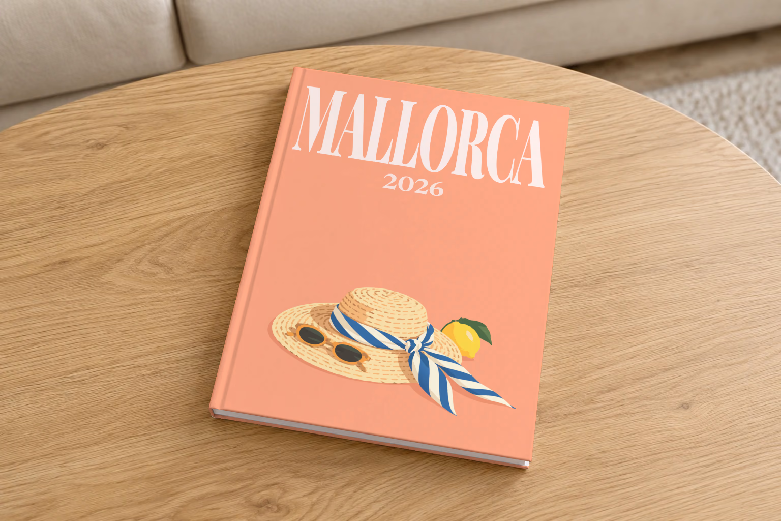 Mallorca hardcover photo book with the illustrated cover of a straw hat with a striped scarf and a lemon on peach, on a round oak coffee table in a bright living room