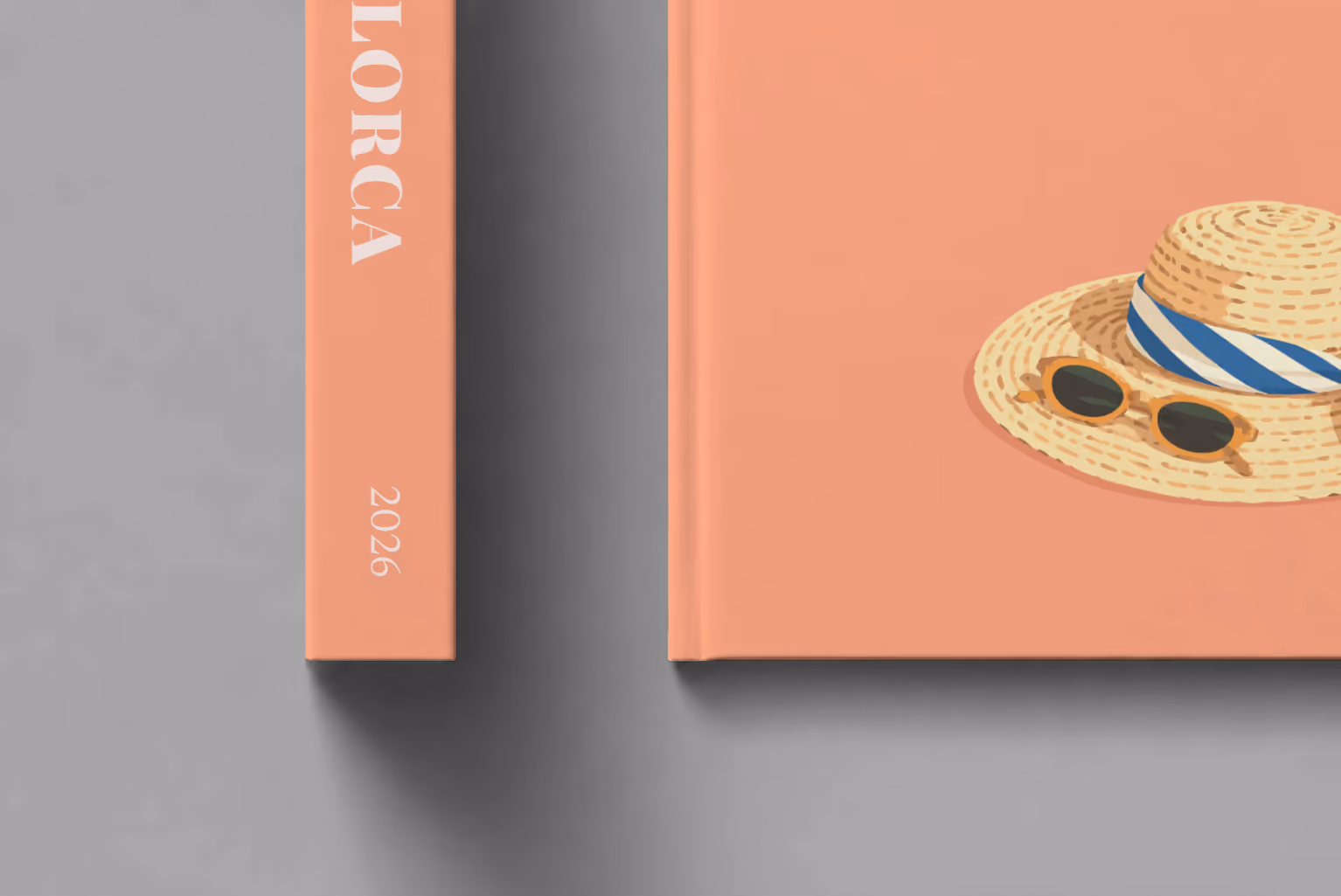 Mallorca hardcover photo book with the illustrated cover of a straw hat with a striped scarf and a lemon on peach, shown close up beside its spine on a pale grey studio surface