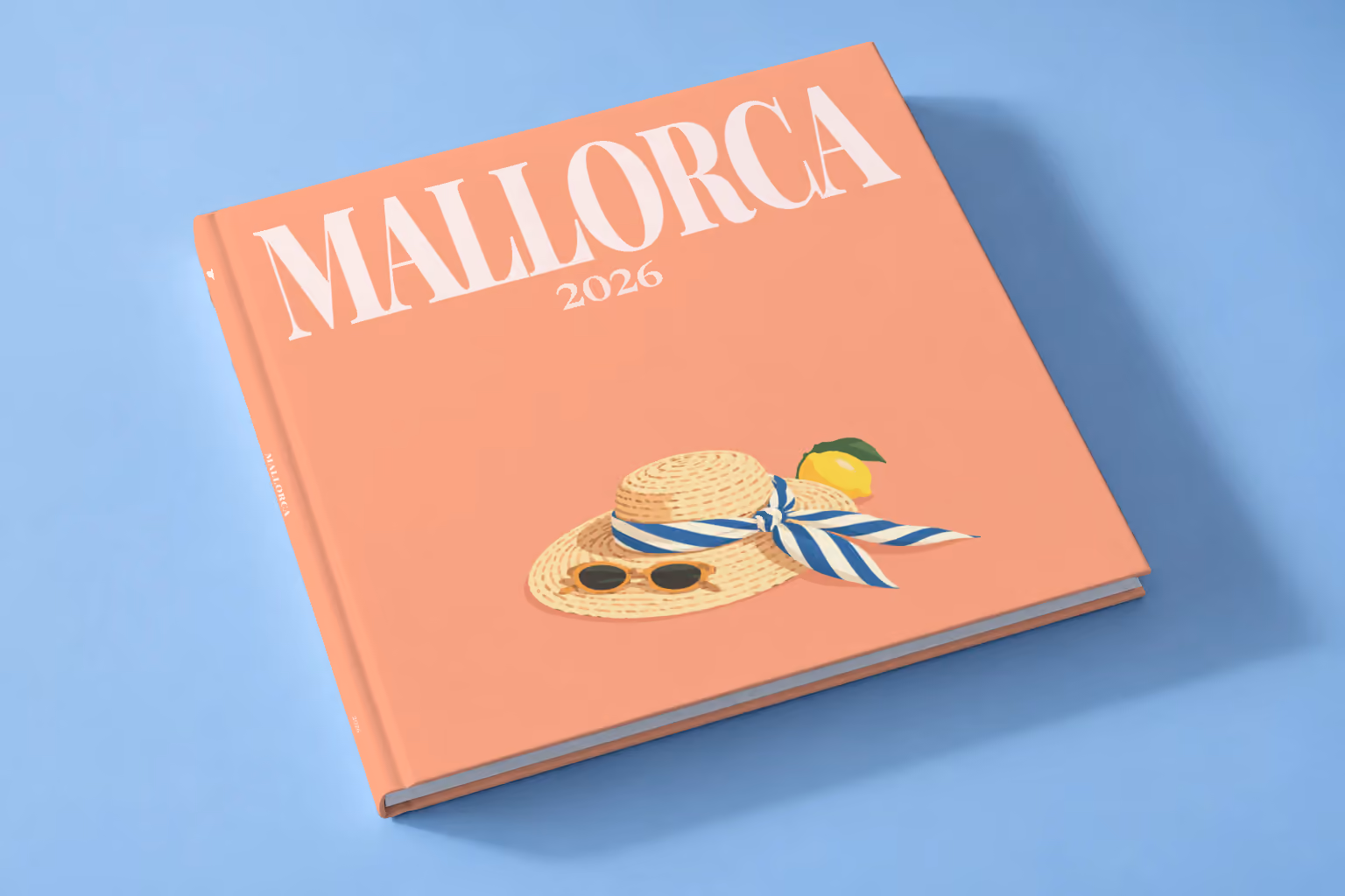 Mallorca square hardcover photo book with the illustrated cover of a straw hat with a striped scarf and a lemon on peach, lying on a pale blue studio backdrop