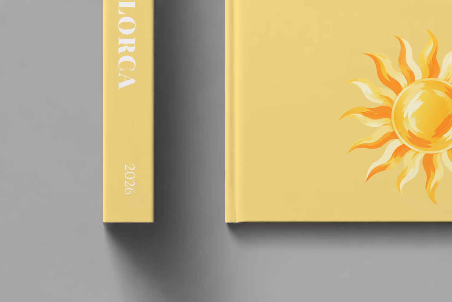Mallorca hardcover photo book with the illustrated cover of a golden sun on pale yellow, shown close up beside its spine on a pale grey studio surface