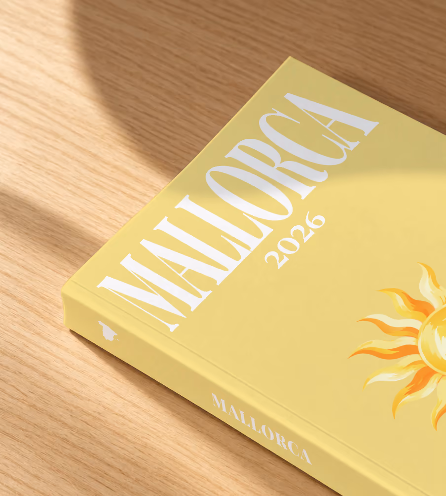 Mallorca softcover photo book with the illustrated cover of a golden sun on pale yellow, lying on an oak desk in dappled afternoon sunlight