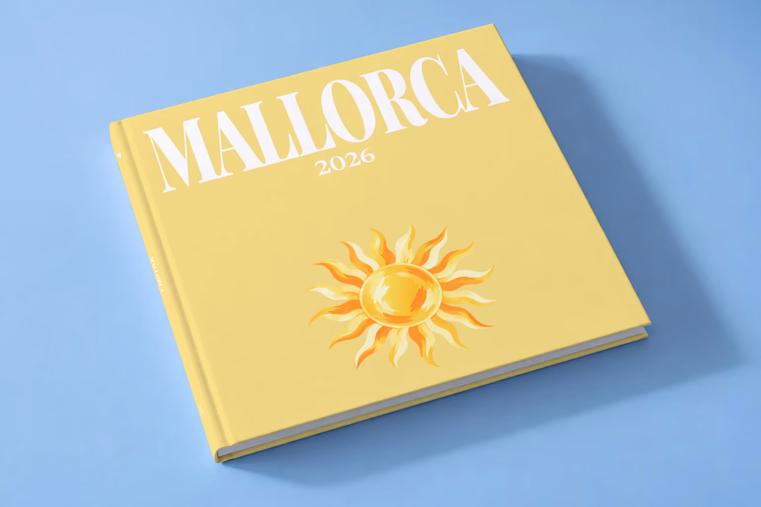 Mallorca square hardcover photo book with the illustrated cover of a golden sun on pale yellow, lying on a pale blue studio backdrop