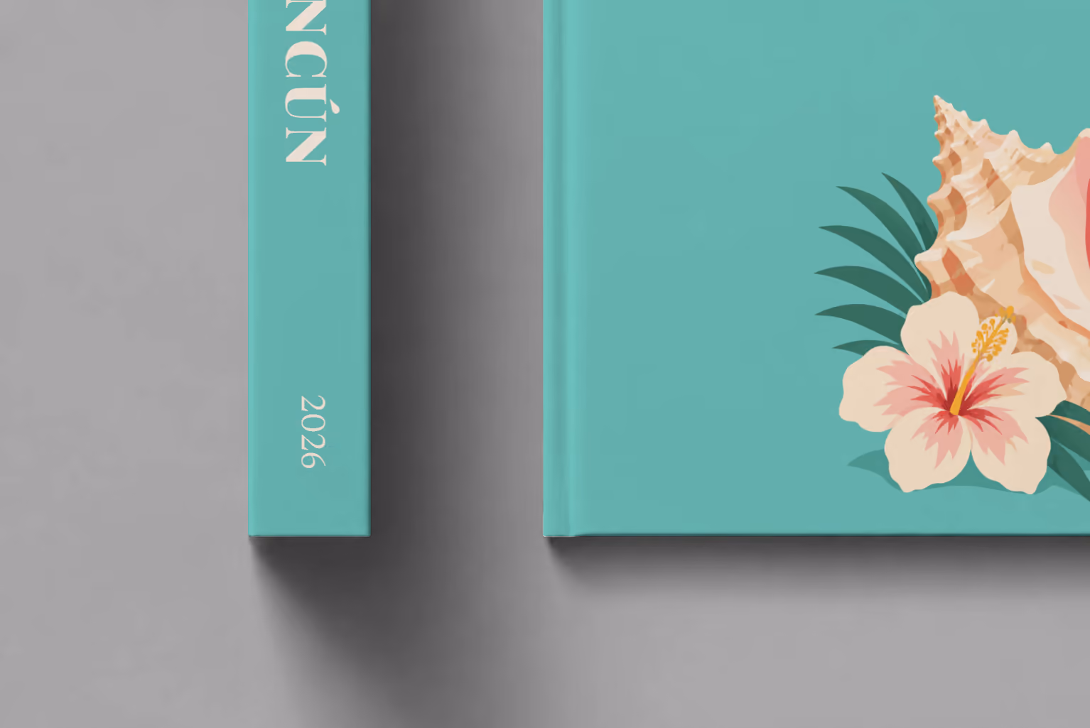 Mexico hardcover photo book with the Cancún illustrated cover of a conch shell and hibiscus on teal, shown close up beside its spine on a pale grey studio surface