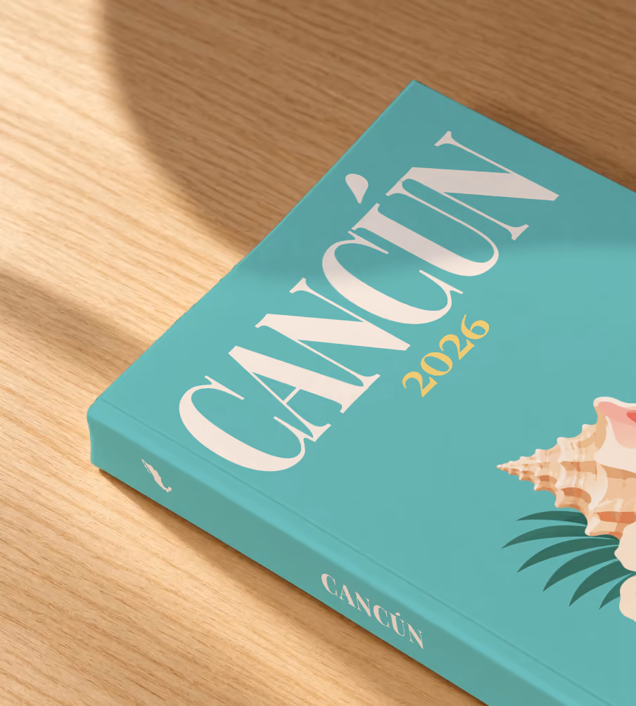 Mexico softcover photo book with the Cancún illustrated cover of a conch shell and hibiscus on teal, lying on an oak desk in dappled afternoon sunlight
