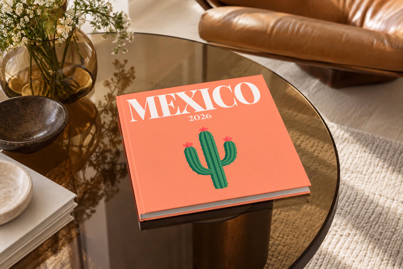 Mexico square hardcover photo book with the illustrated cover of a flowering cactus on coral, on a smoked glass coffee table beside a leather armchair in warm afternoon light