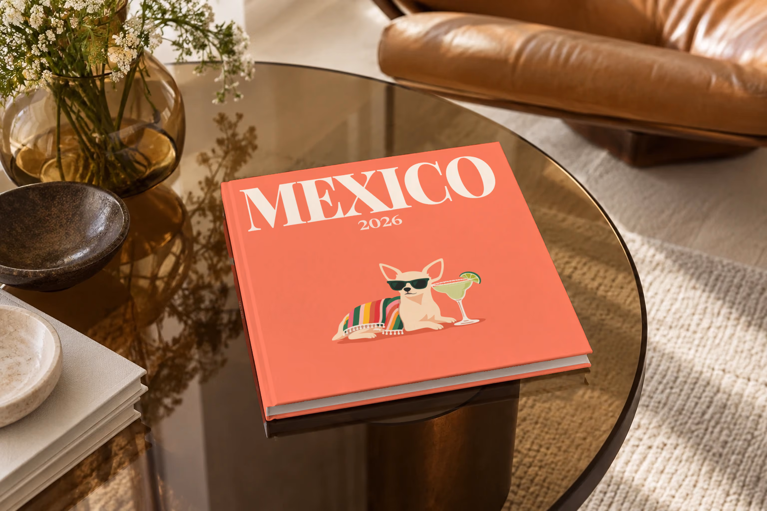 Mexico square hardcover photo book with the illustrated cover of a chihuahua in sunglasses with a margarita on coral, on a smoked glass coffee table beside a leather armchair in warm afternoon light