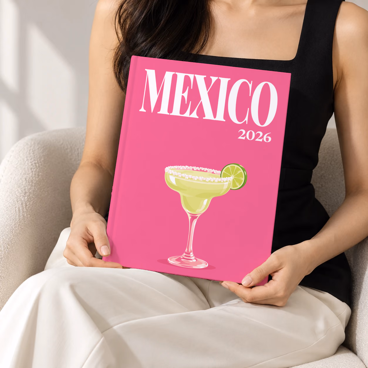 Mexico hardcover photo book with the illustrated cover of a margarita with lime on hot pink, held upright in two hands by a woman in a black top, sitting in a cream boucle armchair