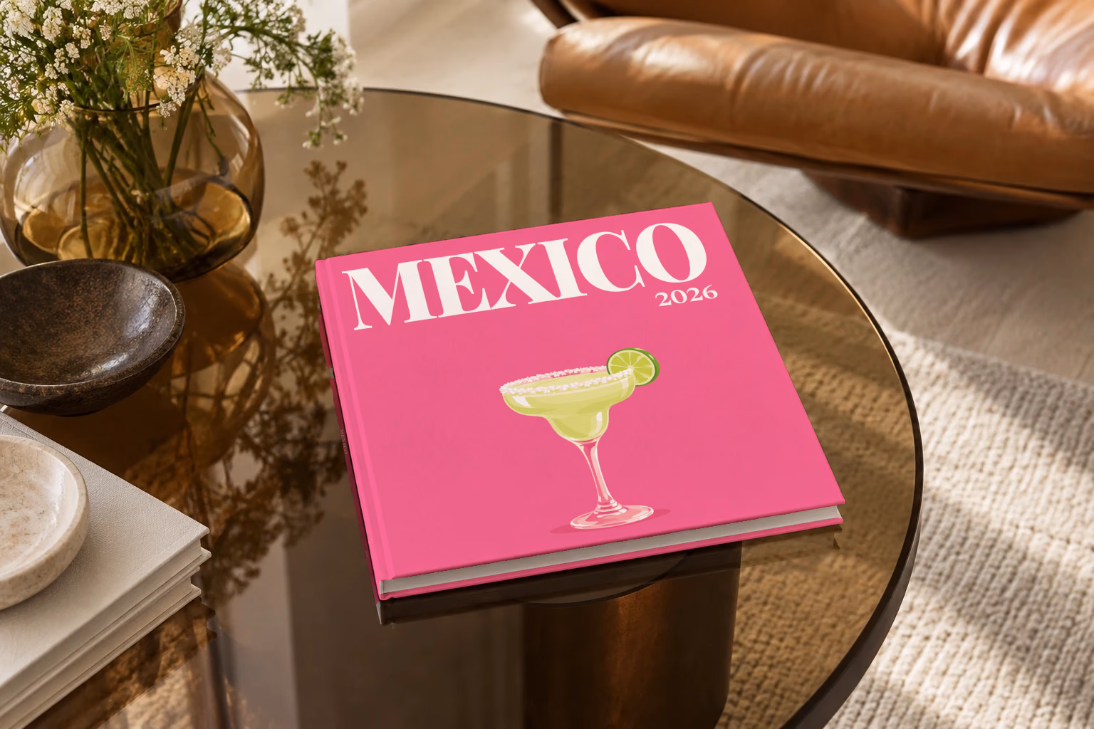 Mexico square hardcover photo book with the illustrated cover of a margarita with lime on hot pink, on a smoked glass coffee table beside a leather armchair in warm afternoon light