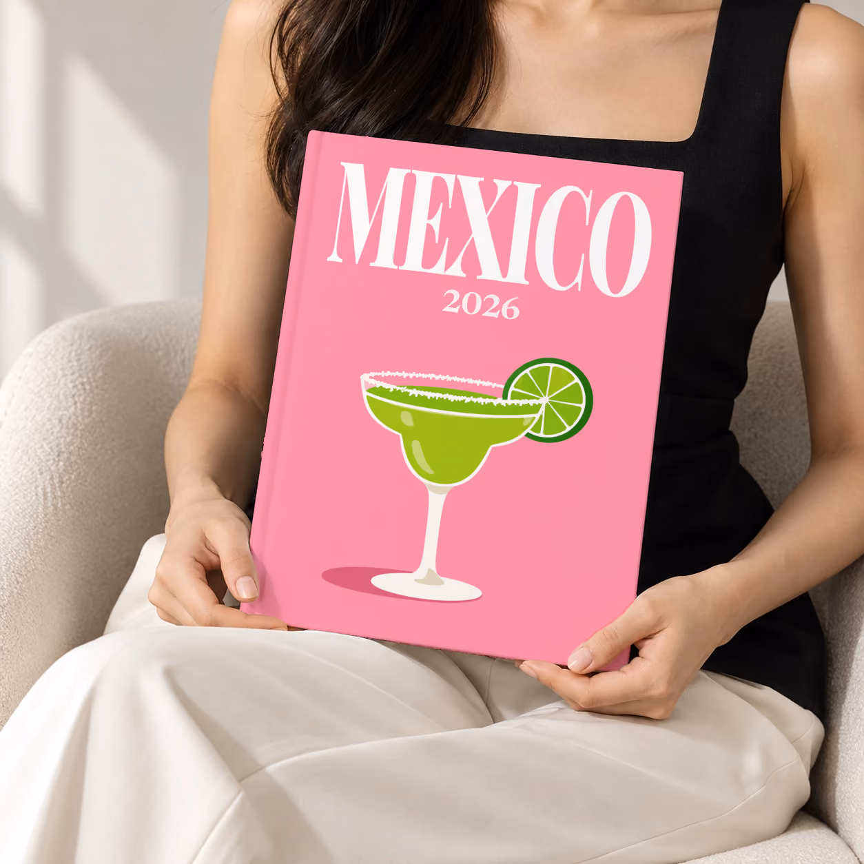 Mexico hardcover photo book with the illustrated cover of a margarita with lime on pink, held upright in two hands by a woman in a black top, sitting in a cream boucle armchair
