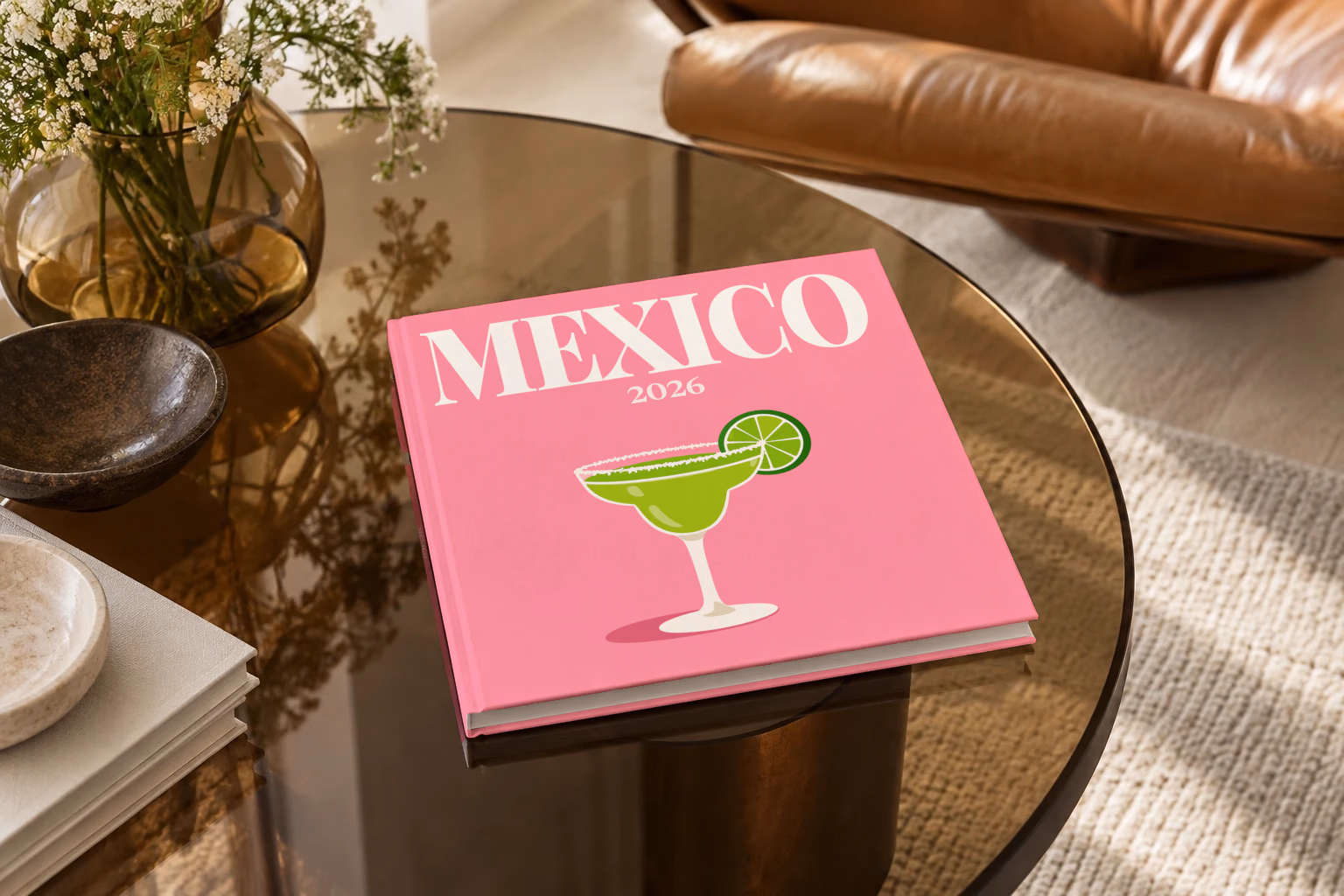 Mexico square hardcover photo book with the illustrated cover of a margarita with lime on pink, on a smoked glass coffee table beside a leather armchair in warm afternoon light