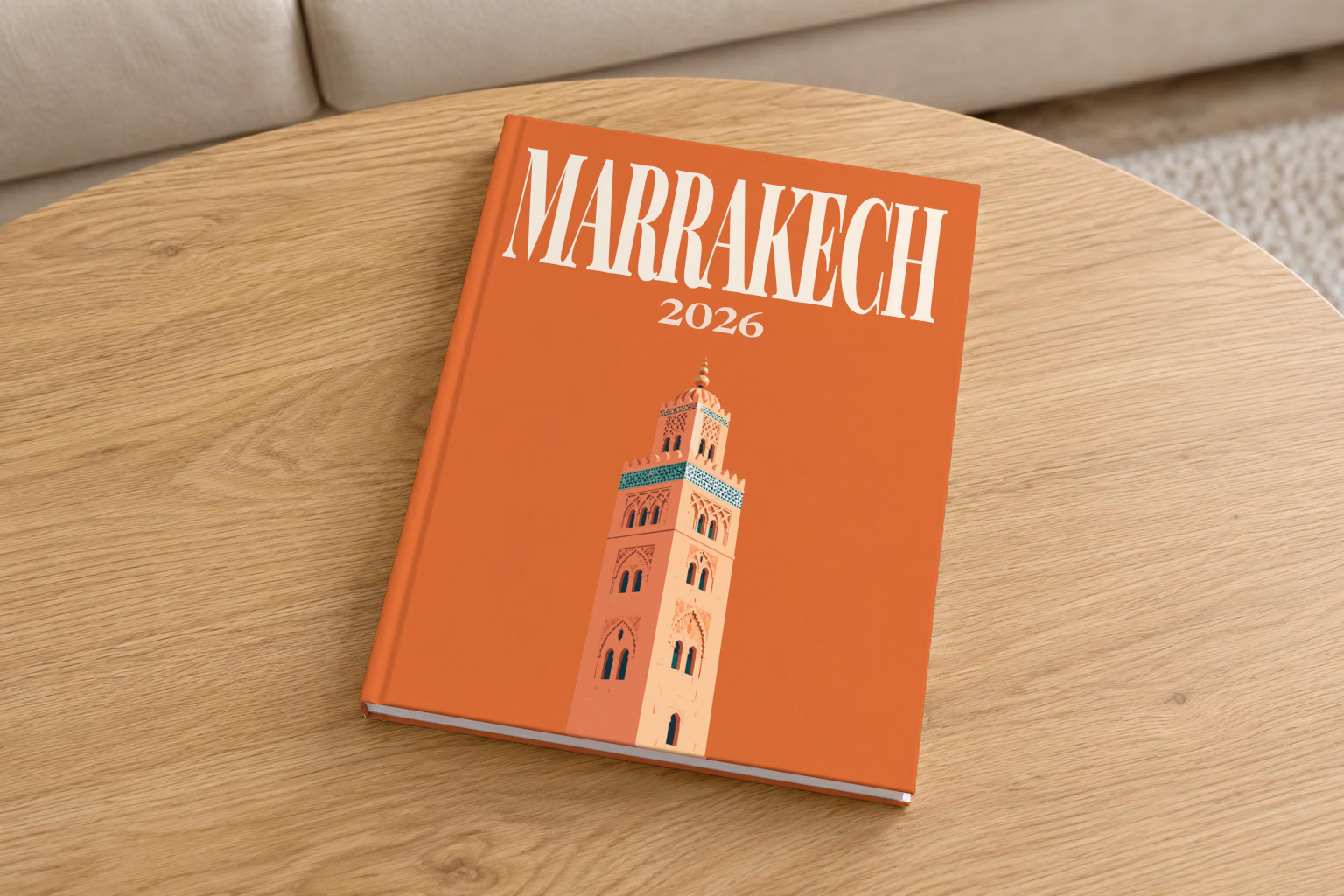 Morocco hardcover photo book with the Marrakech illustrated cover of the Koutoubia Mosque minaret on burnt orange, on a round oak coffee table in a bright living room