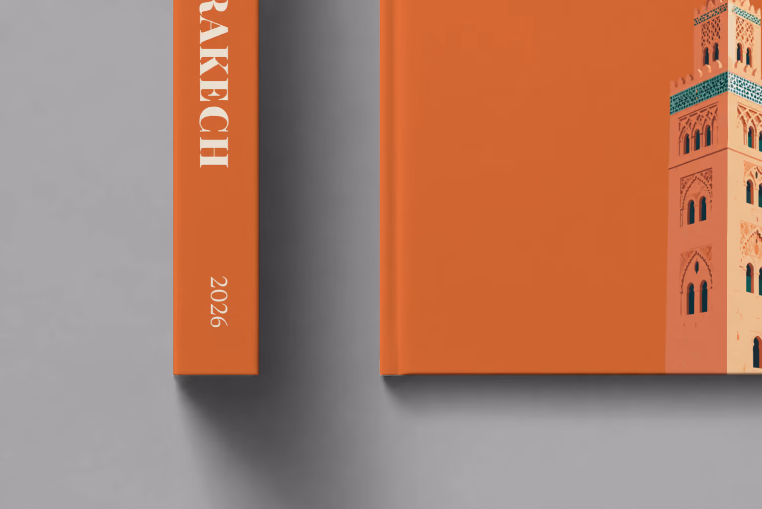 Morocco hardcover photo book with the Marrakech illustrated cover of the Koutoubia Mosque minaret on burnt orange, shown close up beside its spine on a pale grey studio surface
