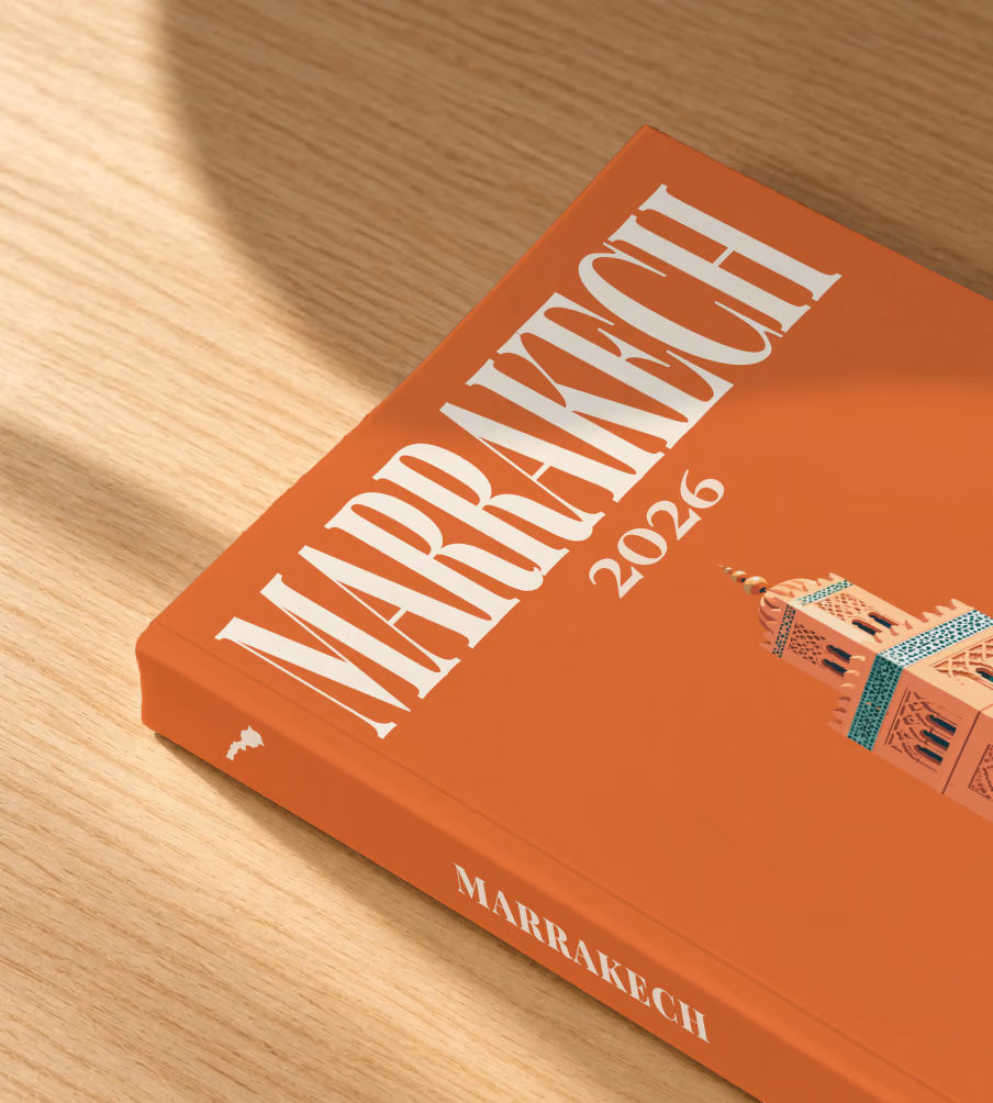 Morocco softcover photo book with the Marrakech illustrated cover of the Koutoubia Mosque minaret on burnt orange, lying on an oak desk in dappled afternoon sunlight