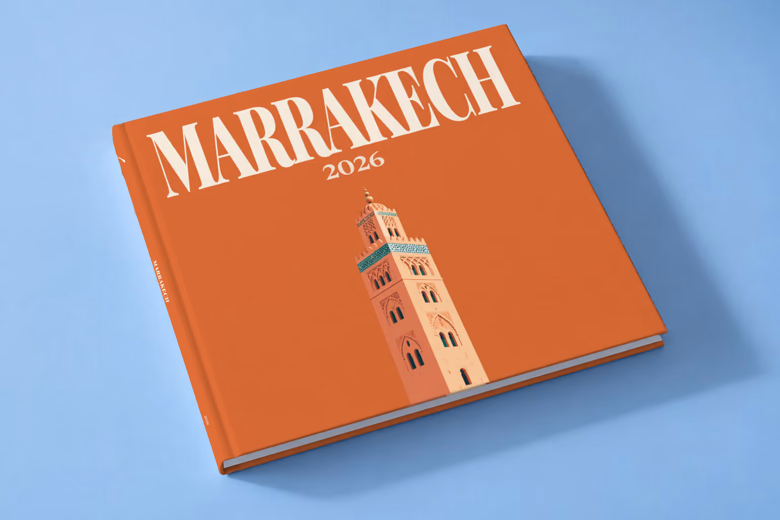 Morocco square hardcover photo book with the Marrakech illustrated cover of the Koutoubia Mosque minaret on burnt orange, lying on a pale blue studio backdrop