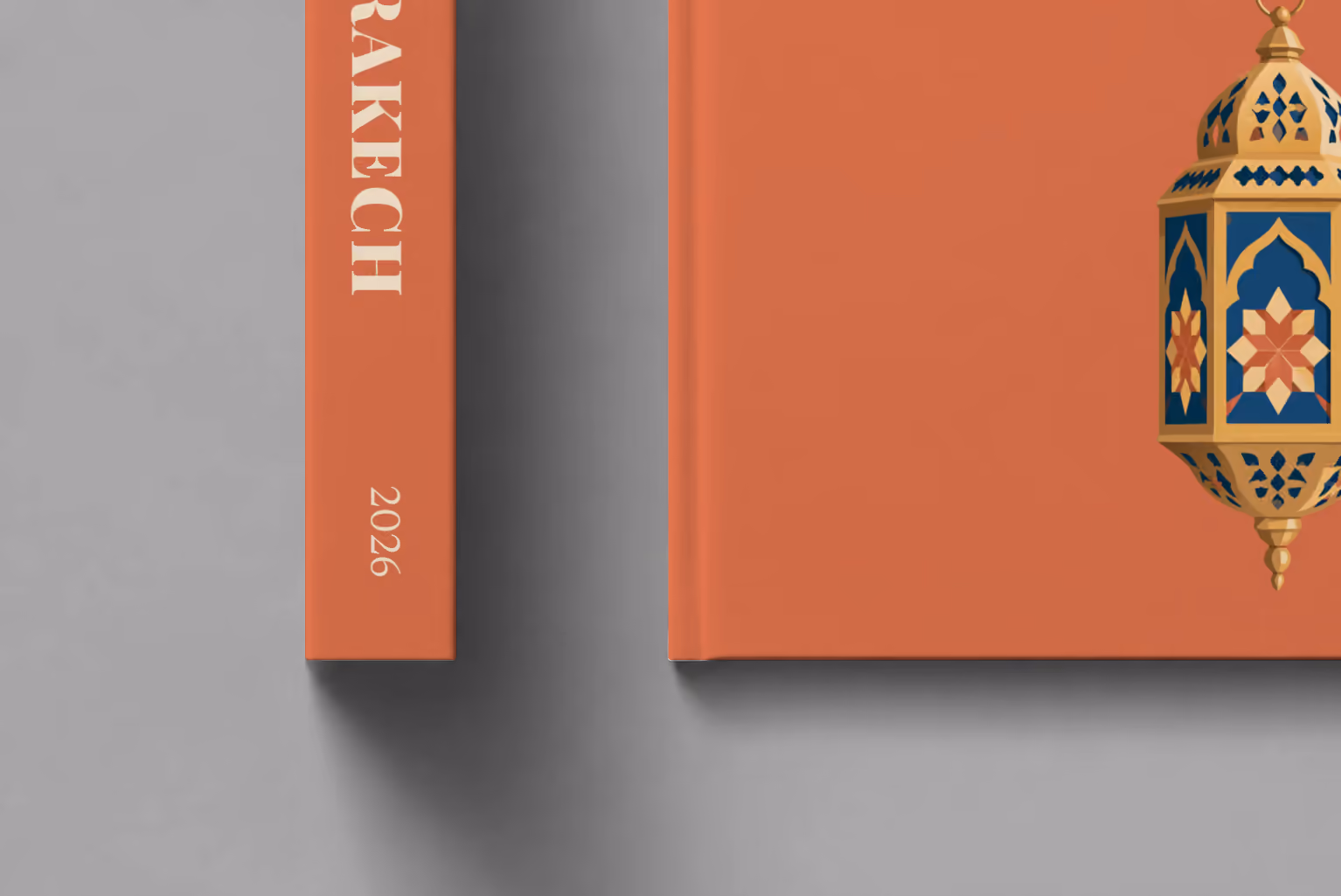 Morocco hardcover photo book with the Marrakech illustrated cover of a gold and blue Moroccan lantern on terracotta, shown close up beside its spine on a pale grey studio surface