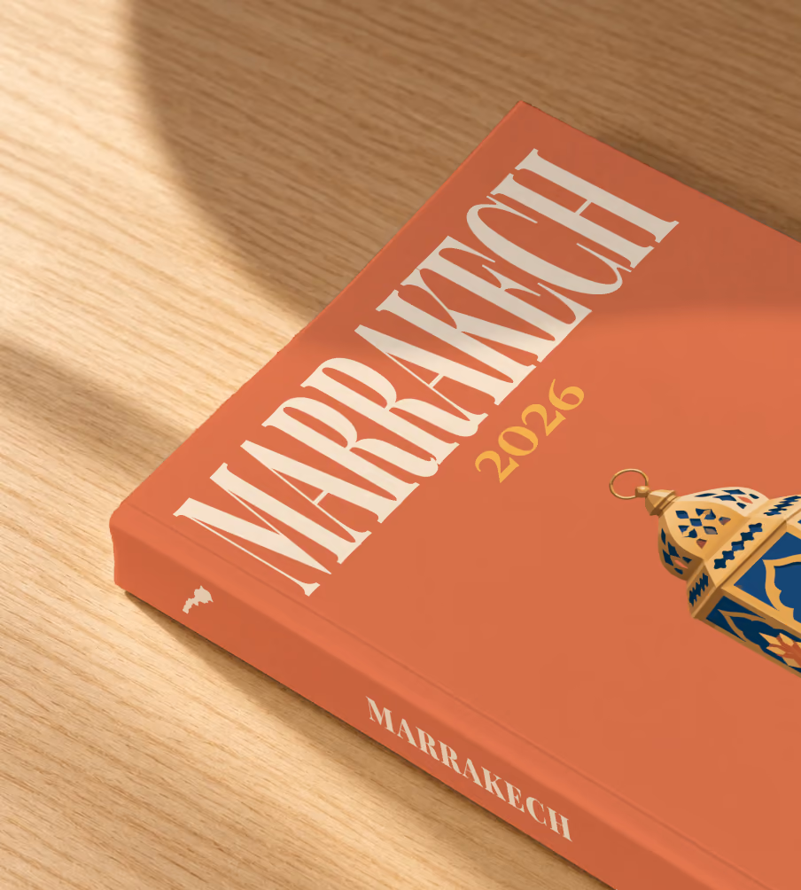 Morocco softcover photo book with the Marrakech illustrated cover of a gold and blue Moroccan lantern on terracotta, lying on an oak desk in dappled afternoon sunlight