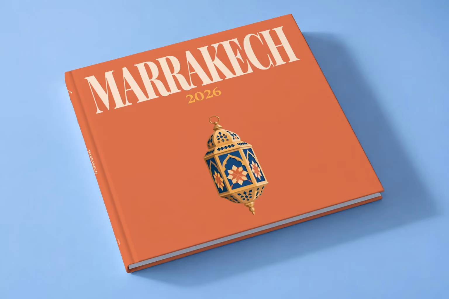 Morocco square hardcover photo book with the Marrakech illustrated cover of a gold and blue Moroccan lantern on terracotta, lying on a pale blue studio backdrop