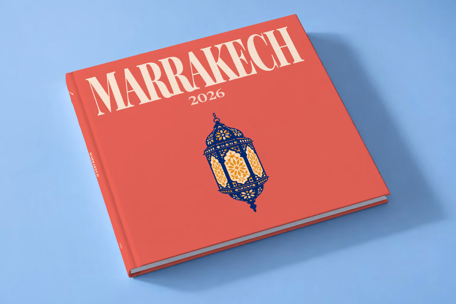 Morocco square hardcover photo book with the Marrakech illustrated cover of a navy and gold Moroccan lantern on red, lying on a pale blue studio backdrop