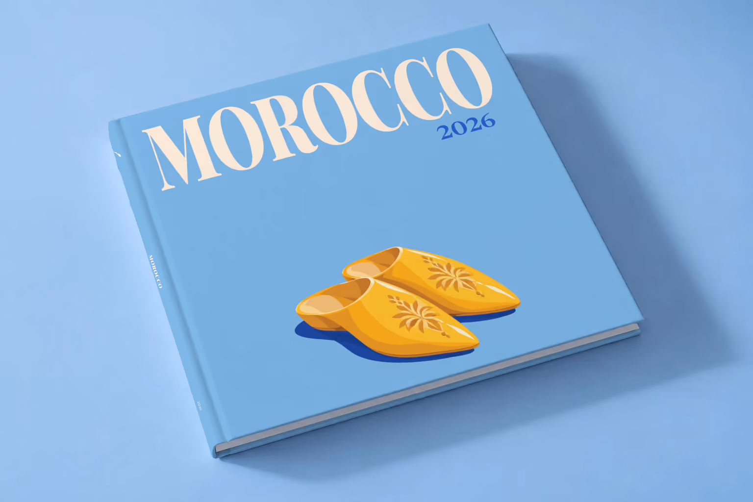Morocco square hardcover photo book with the illustrated cover of a pair of yellow Moroccan babouche slippers on sky blue, lying on a pale blue studio backdrop