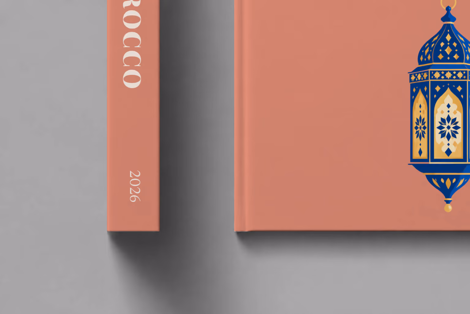 Morocco hardcover photo book with the illustrated cover of a blue and gold Moroccan lantern on dusty terracotta, shown close up beside its spine on a pale grey studio surface
