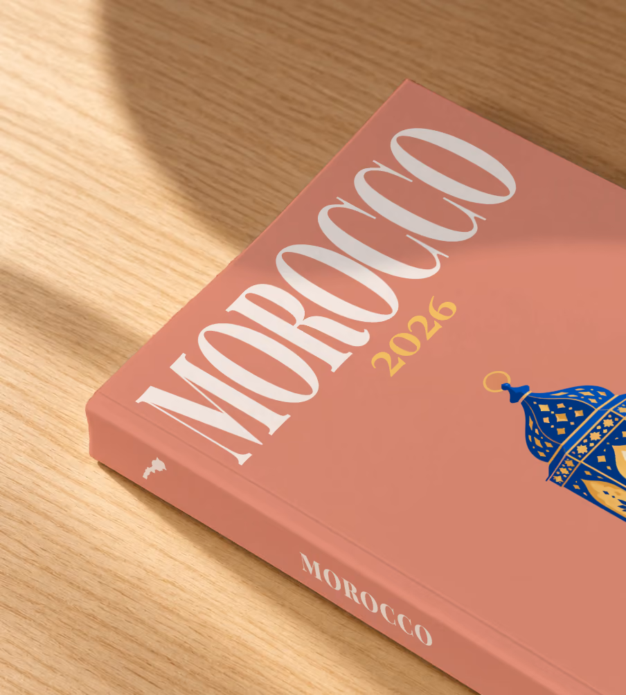 Morocco softcover photo book with the illustrated cover of a blue and gold Moroccan lantern on dusty terracotta, lying on an oak desk in dappled afternoon sunlight