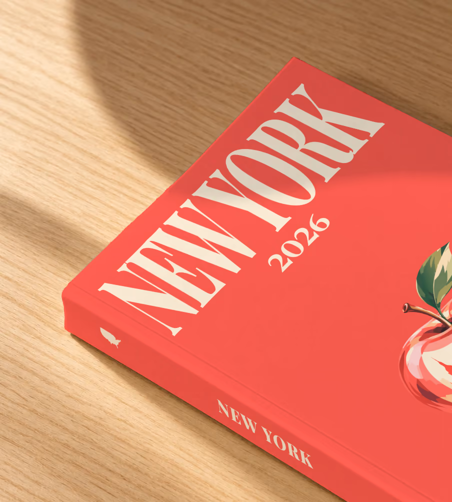 New York softcover photo book with the illustrated cover of a red apple on red, lying on an oak desk in dappled afternoon sunlight