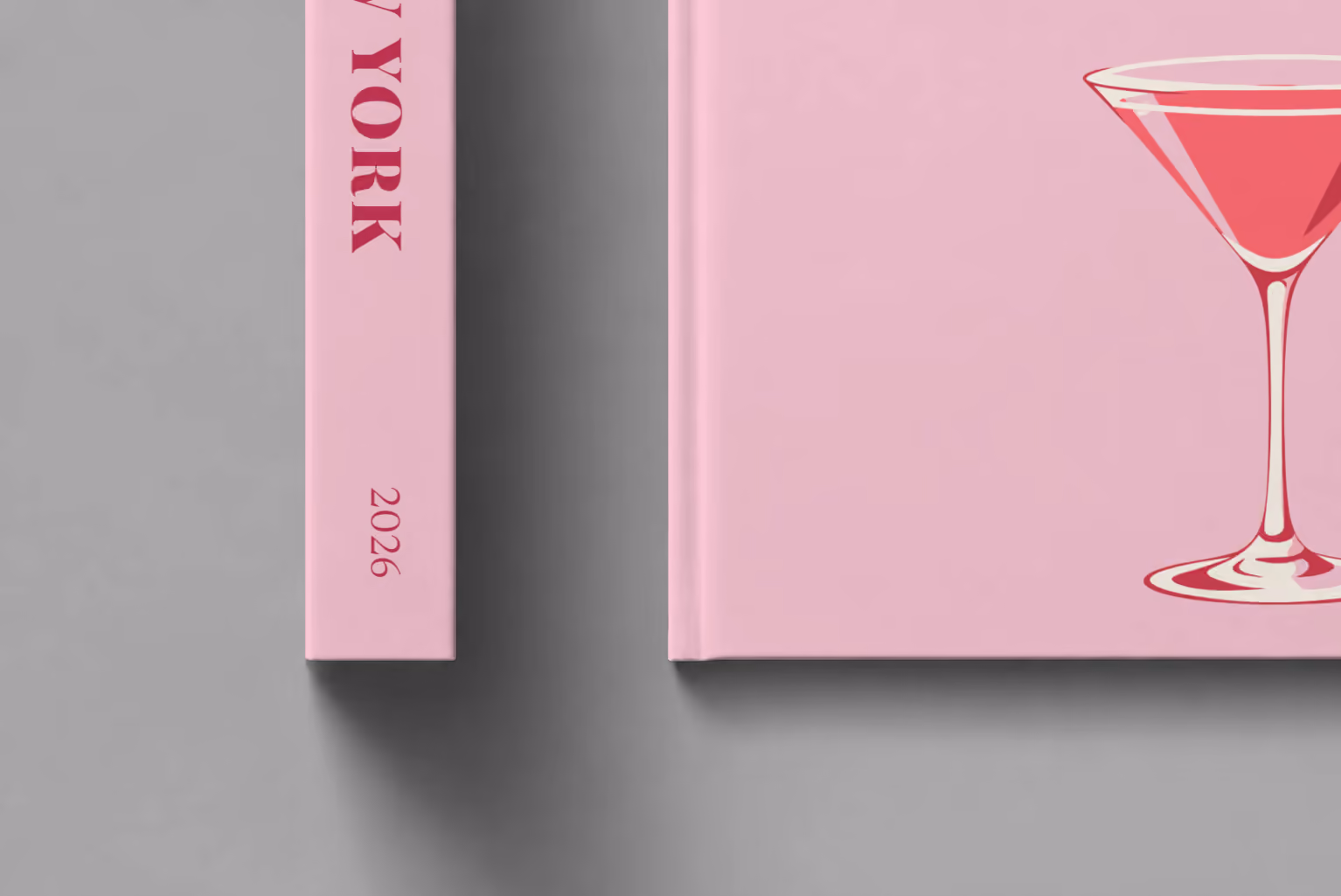New York hardcover photo book with the illustrated cover of a cosmopolitan on pale pink, shown close up beside its spine on a pale grey studio surface