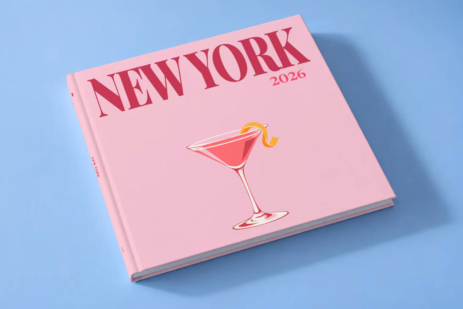 New York square hardcover photo book with the illustrated cover of a cosmopolitan on pale pink, lying on a pale blue studio backdrop