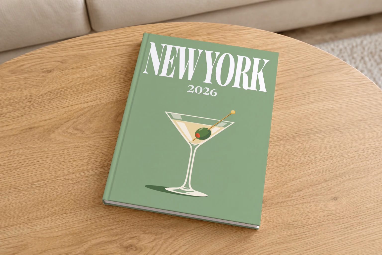 New York hardcover photo book with the illustrated cover of a martini with an olive on sage green, on a round oak coffee table in a bright living room