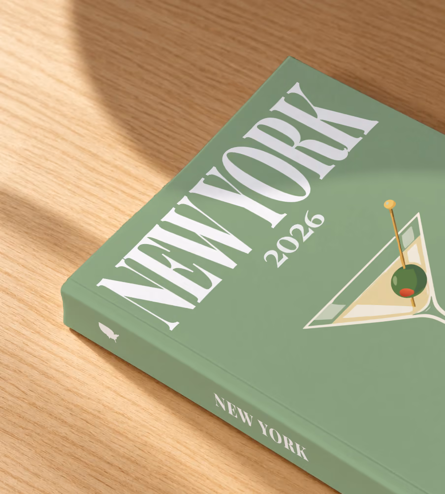 New York softcover photo book with the illustrated cover of a martini with an olive on sage green, lying on an oak desk in dappled afternoon sunlight