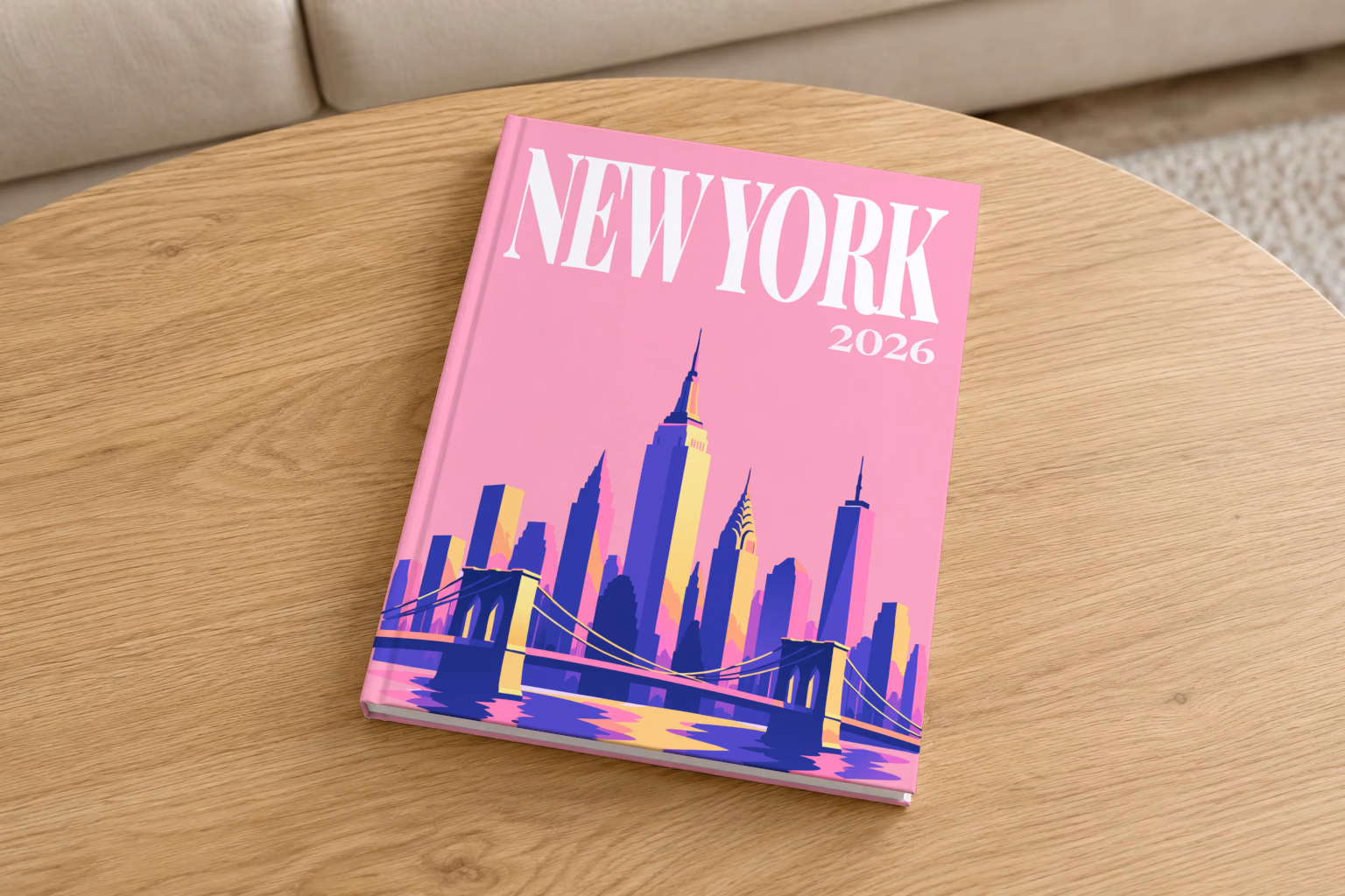 New York hardcover photo book with the illustrated cover of the Manhattan skyline and Brooklyn Bridge on pink, on a round oak coffee table in a bright living room