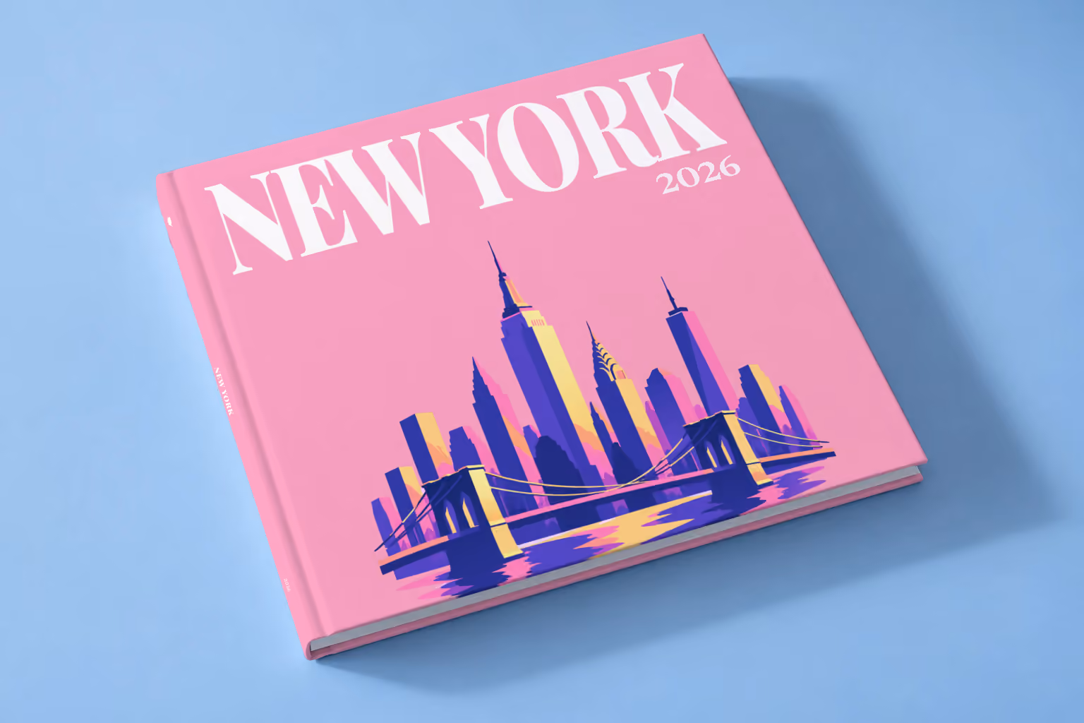 New York square hardcover photo book with the illustrated cover of the Manhattan skyline and Brooklyn Bridge on pink, lying on a pale blue studio backdrop