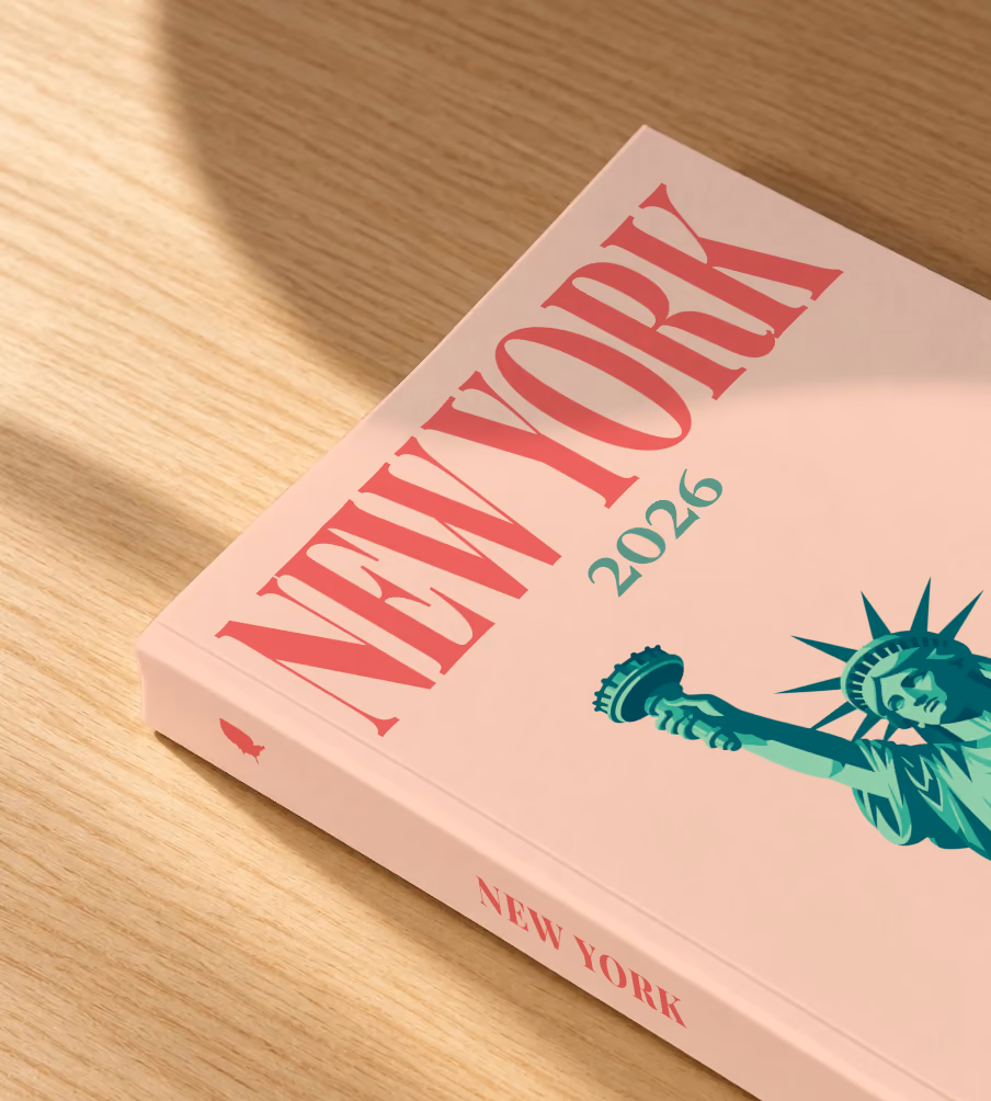 New York softcover photo book with the illustrated cover of the Statue of Liberty on peach, lying on an oak desk in dappled afternoon sunlight