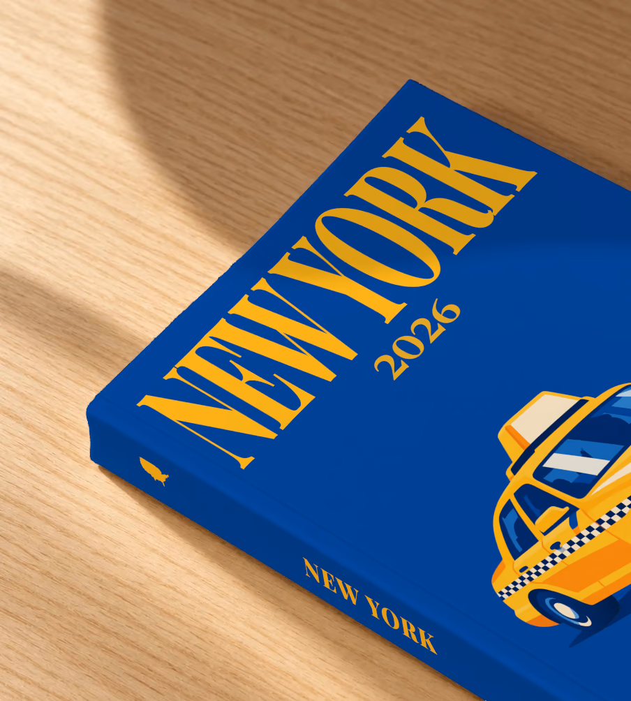 New York softcover photo book with the illustrated cover of a yellow taxi on royal blue, lying on an oak desk in dappled afternoon sunlight