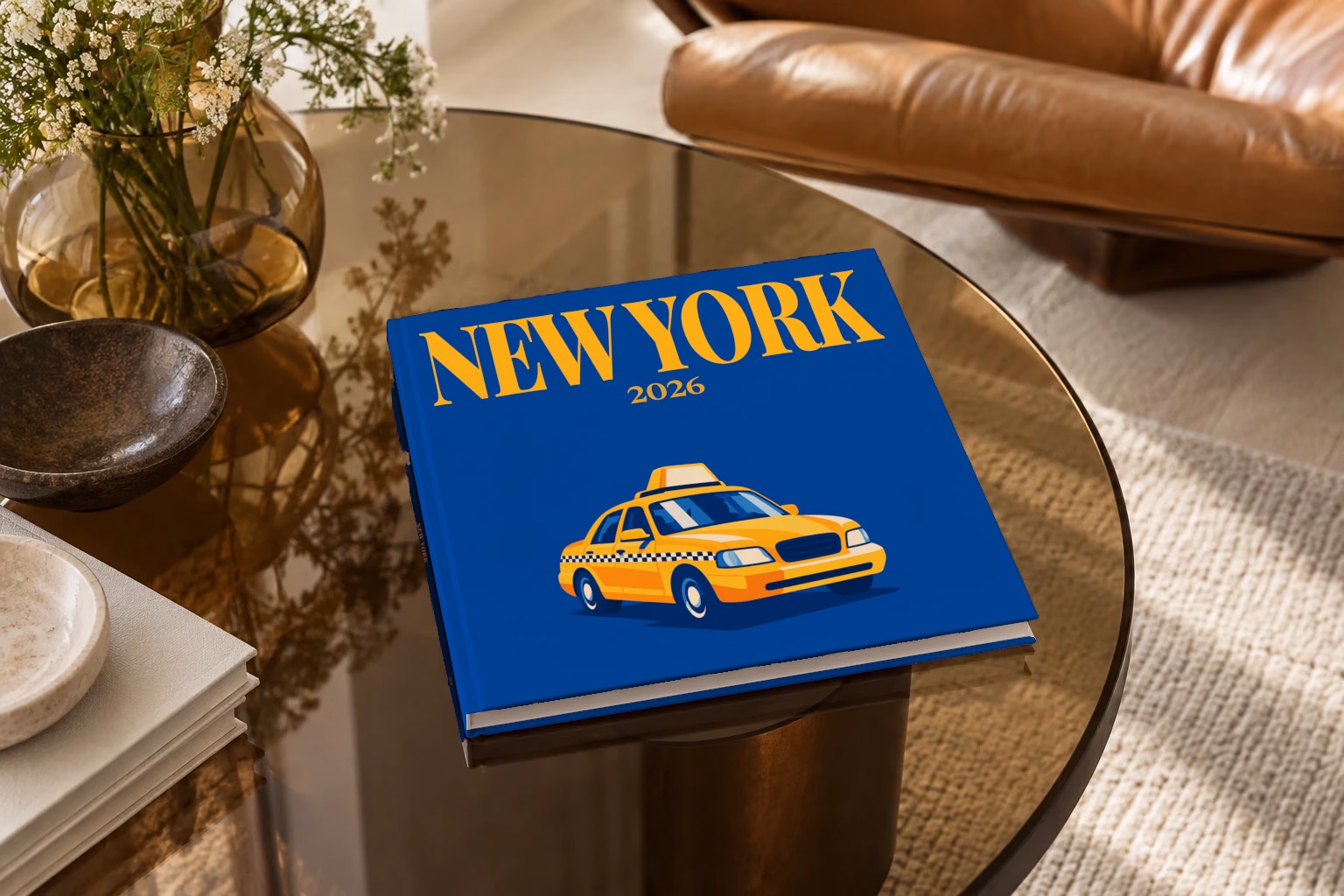 New York square hardcover photo book with the illustrated cover of a yellow taxi on royal blue, on a smoked glass coffee table beside a leather armchair in warm afternoon light