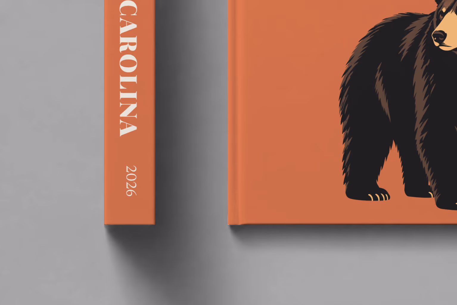 North Carolina hardcover photo book with the illustrated cover of a black bear on burnt orange, shown close up beside its spine on a pale grey studio surface