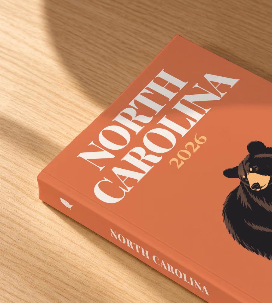 North Carolina softcover photo book with the illustrated cover of a black bear on burnt orange, lying on an oak desk in dappled afternoon sunlight