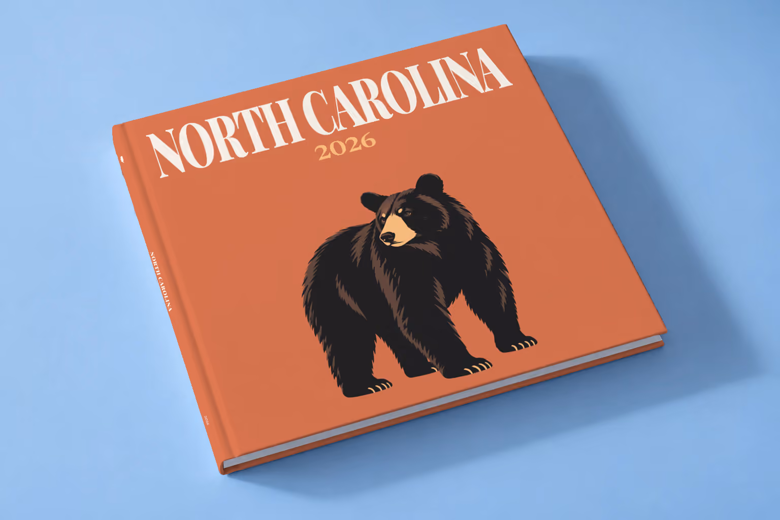 North Carolina square hardcover photo book with the illustrated cover of a black bear on burnt orange, lying on a pale blue studio backdrop