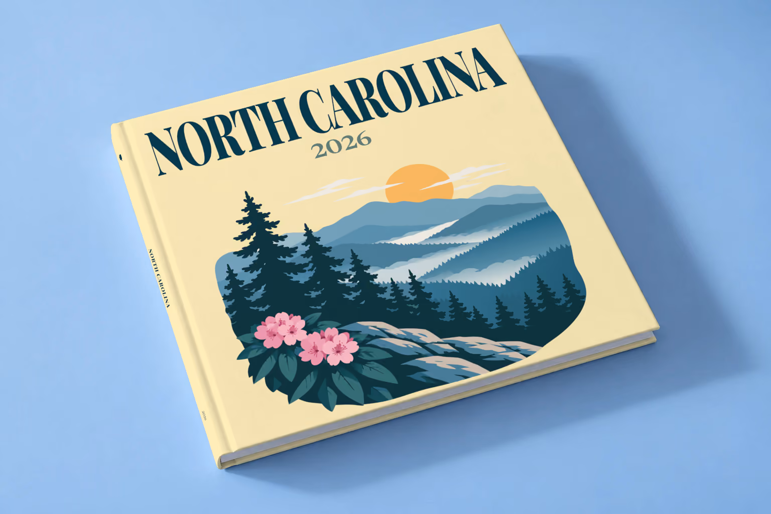 North Carolina square hardcover photo book with the illustrated cover of the Blue Ridge Mountains with pine trees and pink rhododendron on pale yellow, lying on a pale blue studio backdrop