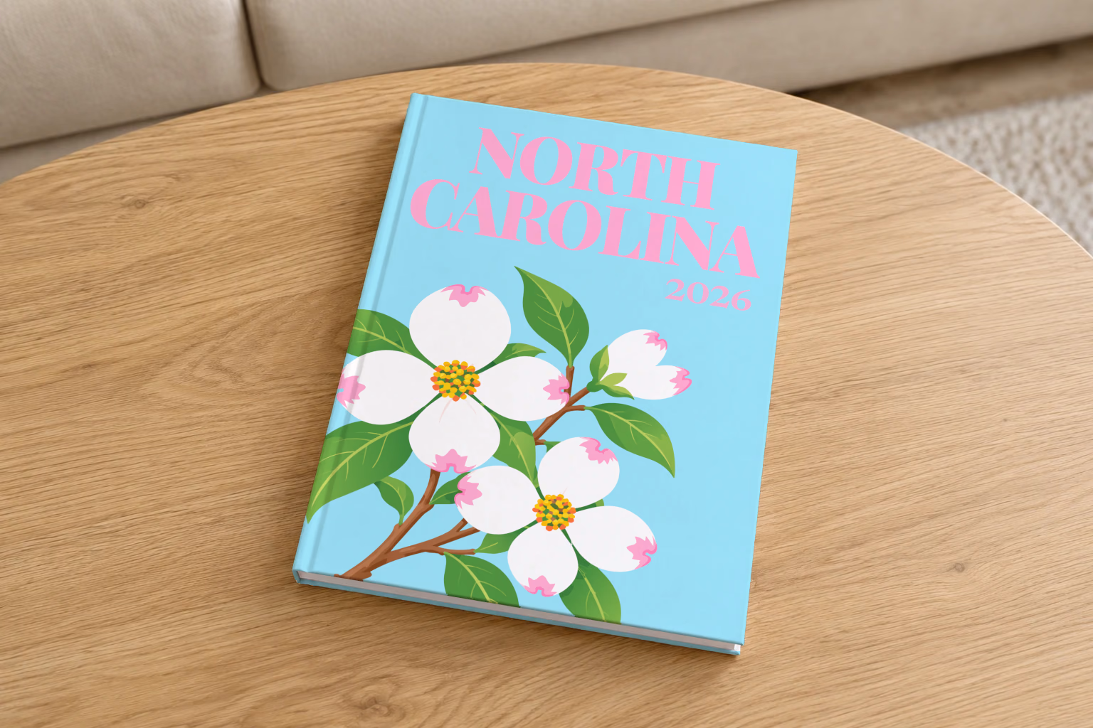 North Carolina hardcover photo book with the illustrated cover of white dogwood blossoms, the state flower, on pale aqua, on a round oak coffee table in a bright living room
