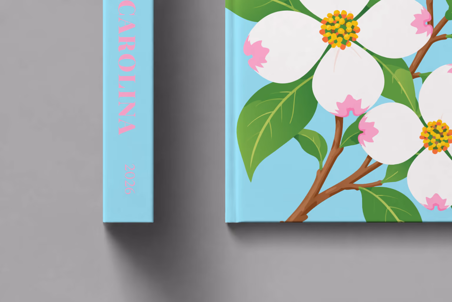 North Carolina hardcover photo book with the illustrated cover of white dogwood blossoms, the state flower, on pale aqua, shown close up beside its spine on a pale grey studio surface