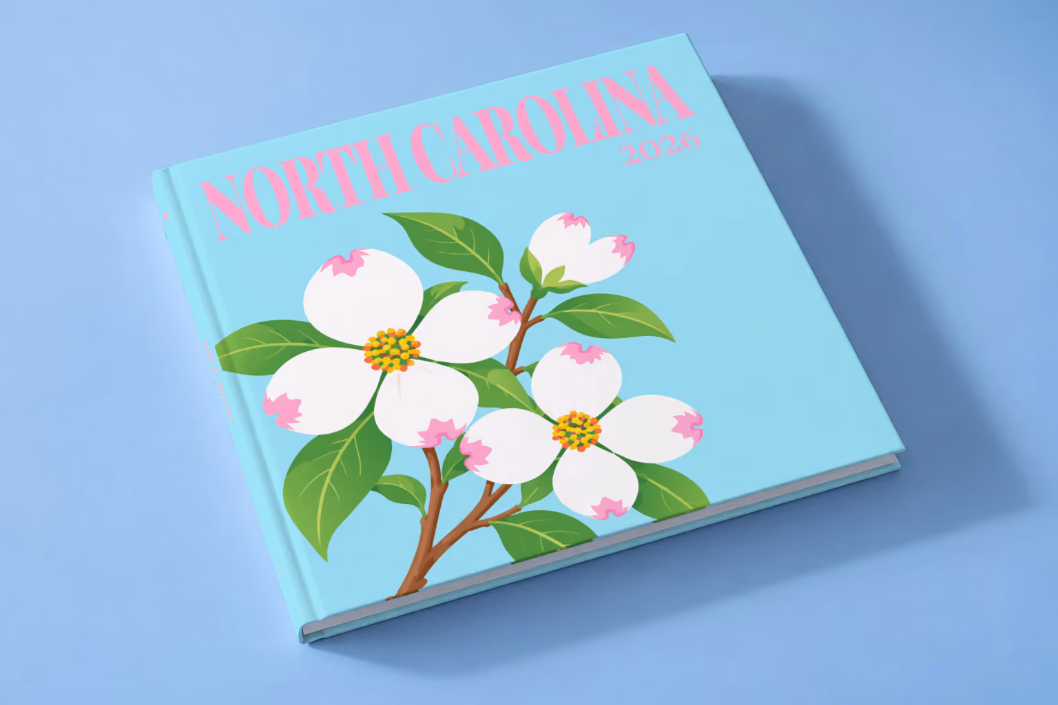 North Carolina square hardcover photo book with the illustrated cover of white dogwood blossoms, the state flower, on pale aqua, lying on a pale blue studio backdrop