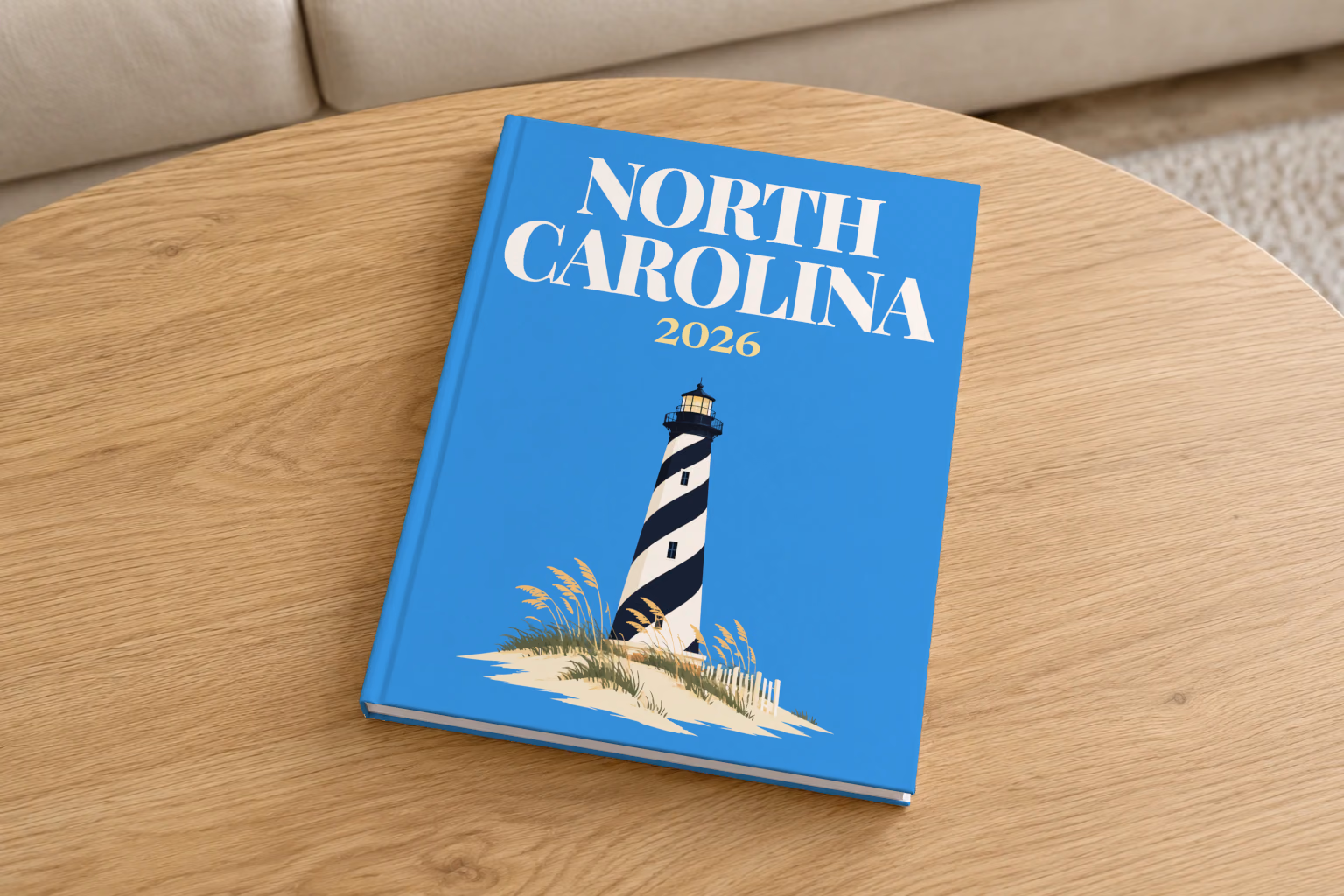 North Carolina hardcover photo book with the illustrated cover of the black and white spiral Cape Hatteras Lighthouse on the dunes on blue, on a round oak coffee table in a bright living room