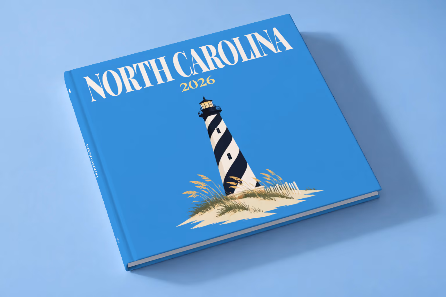 North Carolina square hardcover photo book with the illustrated cover of the black and white spiral Cape Hatteras Lighthouse on the dunes on blue, lying on a pale blue studio backdrop