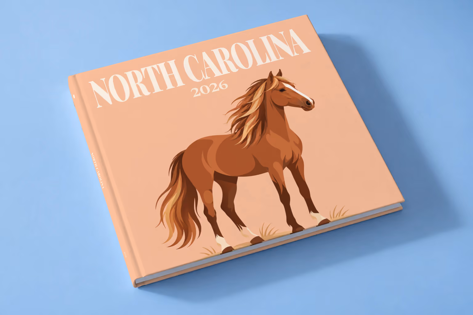 North Carolina square hardcover photo book with the illustrated cover of a wild Outer Banks horse on peach, lying on a pale blue studio backdrop