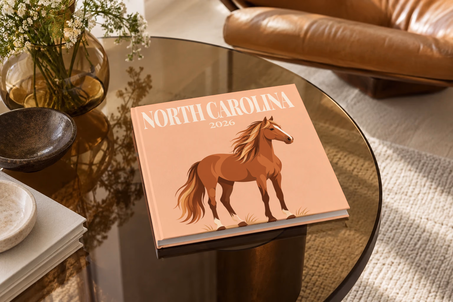 North Carolina square hardcover photo book with the illustrated cover of a wild Outer Banks horse on peach, on a smoked glass coffee table beside a leather armchair in warm afternoon light