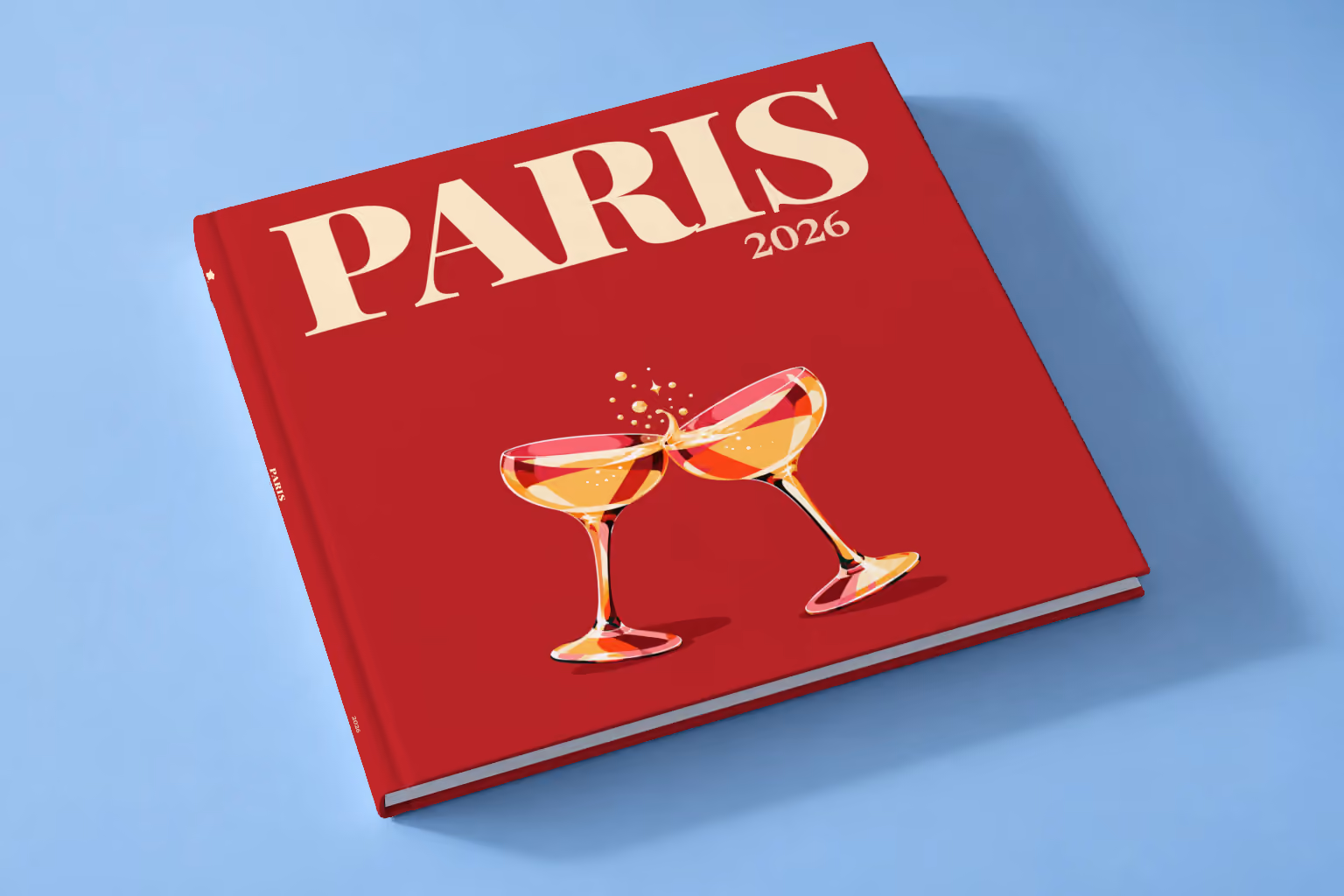 Paris square hardcover photo book with the illustrated cover of two champagne coupes on deep red, lying on a pale blue studio backdrop