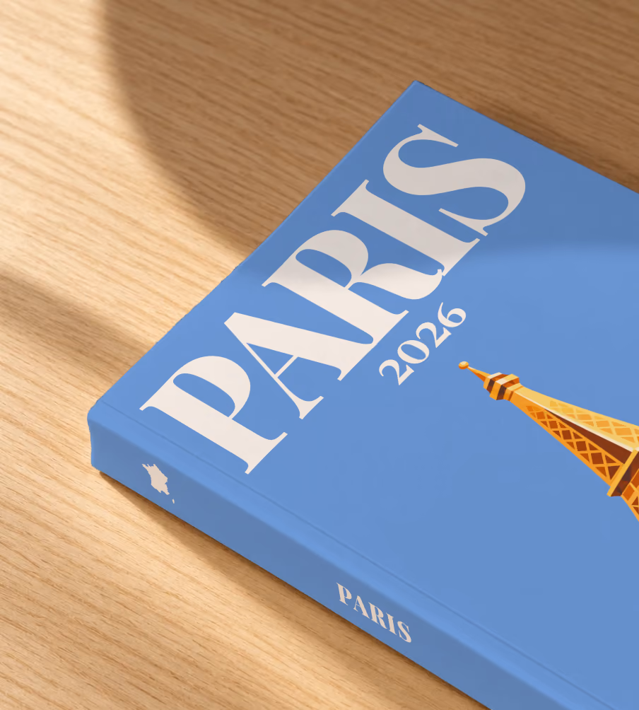Paris softcover photo book with the illustrated cover of a gold Eiffel Tower on blue, lying on an oak desk in dappled afternoon sunlight
